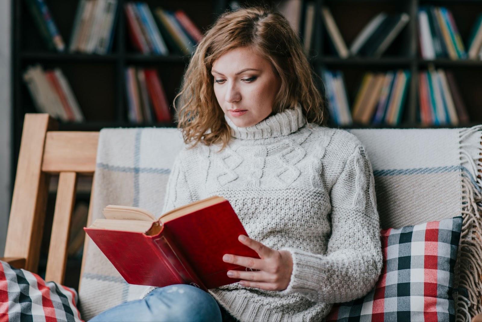 A woman in a sweater sitting on a couch reading a book