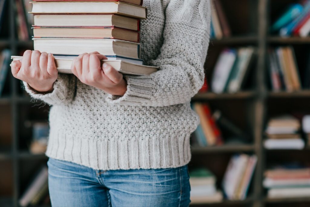 A woman carries a stack of books