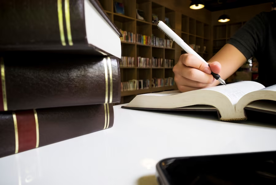 Woman using fountain pen to write on paper next to books