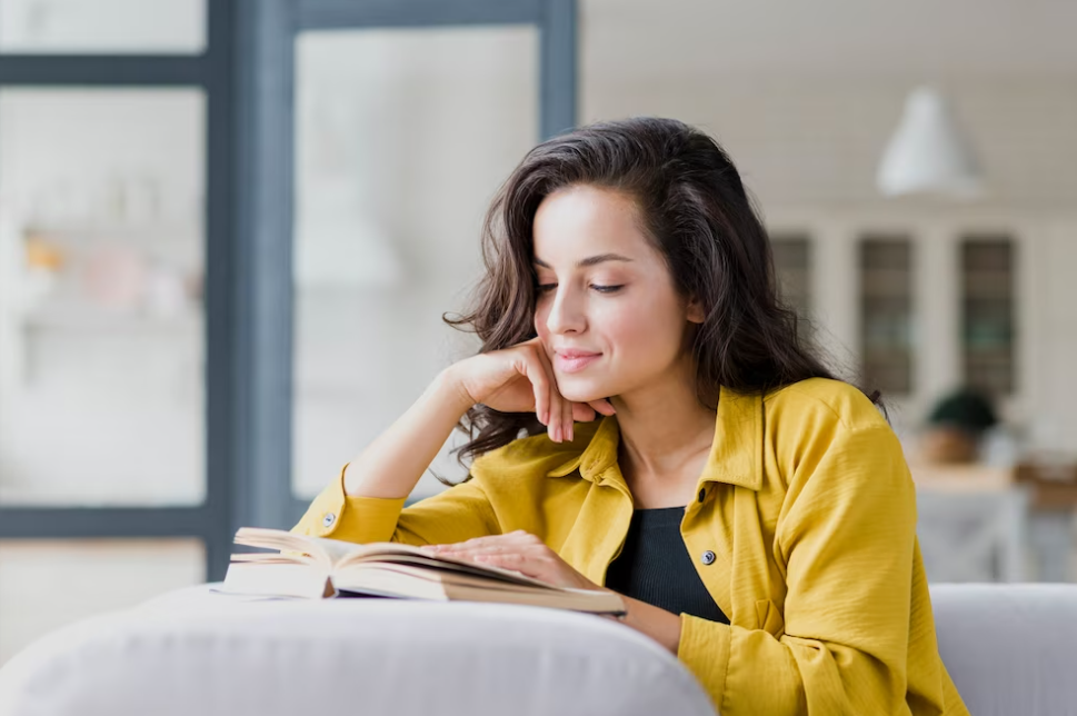 woman in yellow shirt reading book and smiling on a coach